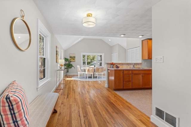 kitchen with visible vents, brown cabinets, light wood-style floors, light countertops, and vaulted ceiling