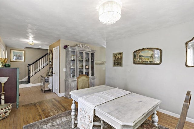 dining area with stairs, baseboards, a chandelier, and hardwood / wood-style flooring