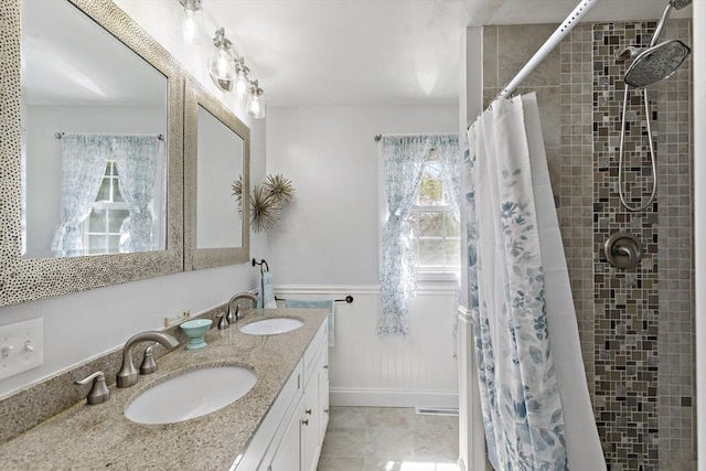 bathroom with a sink, a wainscoted wall, double vanity, and tiled shower
