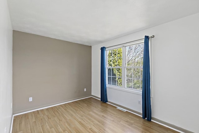 empty room featuring visible vents, light wood-style flooring, and baseboards