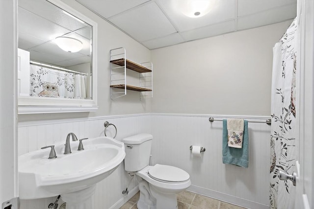 bathroom with a sink, a wainscoted wall, toilet, and a paneled ceiling