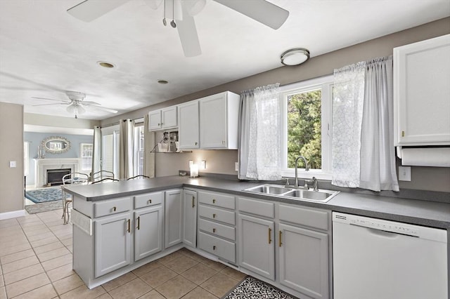 kitchen featuring white dishwasher, a sink, a ceiling fan, a peninsula, and light tile patterned floors