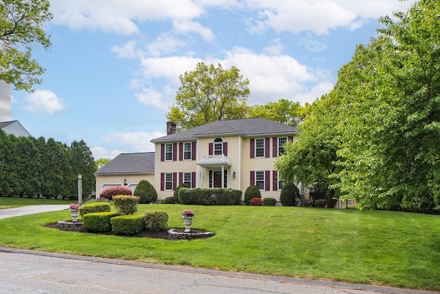 colonial home with a chimney, a front yard, a garage, and driveway