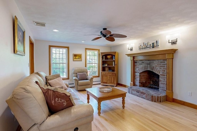living room with light wood finished floors, ceiling fan, baseboard heating, a fireplace, and baseboards