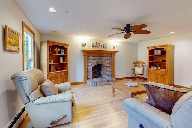 living room featuring a baseboard heating unit, light wood-style flooring, a ceiling fan, recessed lighting, and a brick fireplace