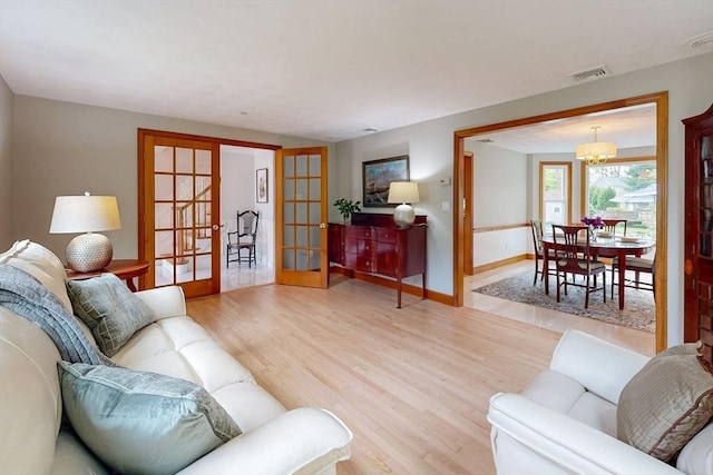 living room with french doors, light wood-style flooring, baseboards, and a chandelier