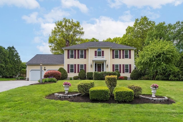 colonial home with a chimney, a front yard, a garage, and concrete driveway