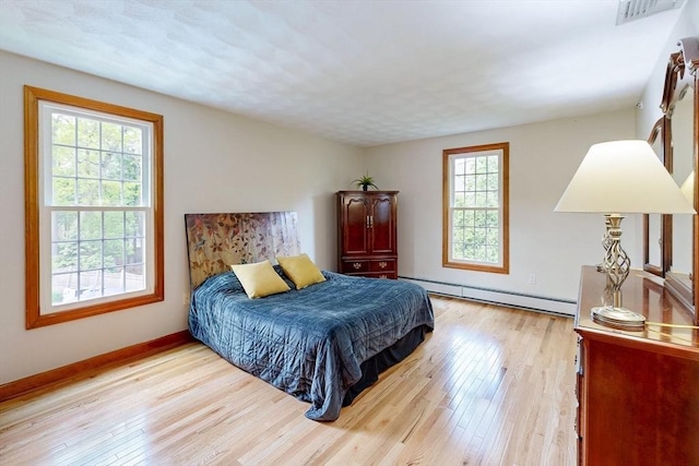bedroom featuring baseboard heating, light wood finished floors, and baseboards