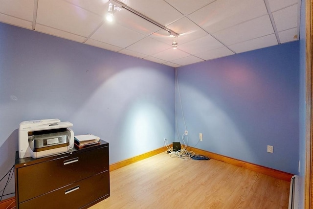 unfurnished room featuring wood finished floors, rail lighting, baseboards, a baseboard radiator, and a drop ceiling
