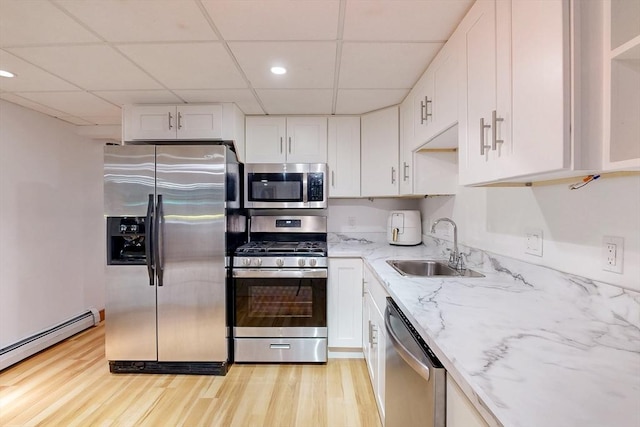 kitchen featuring appliances with stainless steel finishes, a drop ceiling, baseboard heating, a sink, and light stone countertops