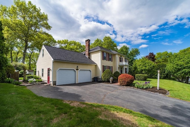 colonial-style house featuring an attached garage, a chimney, asphalt driveway, and a front yard
