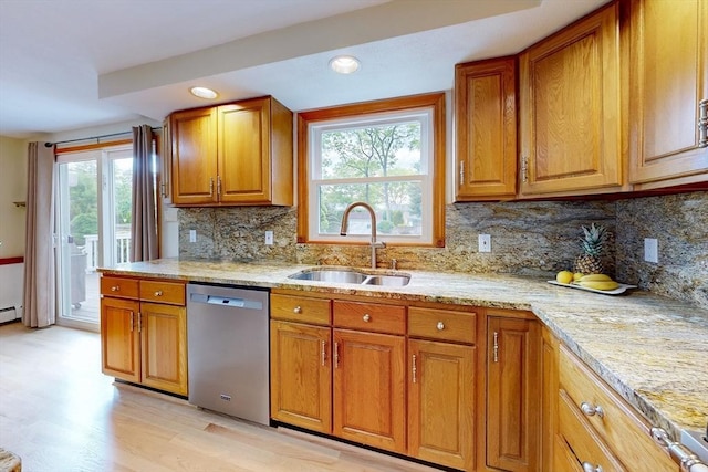 kitchen with stainless steel dishwasher, a sink, brown cabinets, light wood-style flooring, and light stone countertops