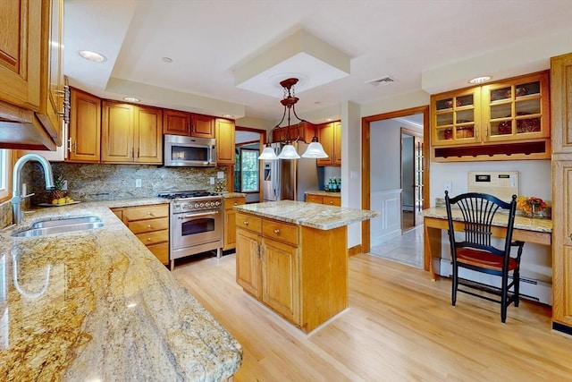 kitchen with stainless steel appliances, a sink, a center island, light wood finished floors, and light stone counters