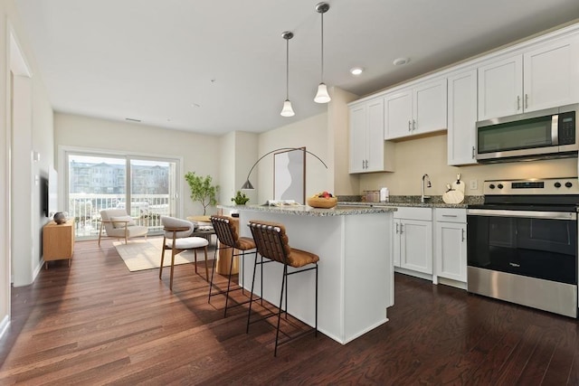 kitchen featuring white cabinetry, dark wood-type flooring, hanging light fixtures, light stone counters, and appliances with stainless steel finishes