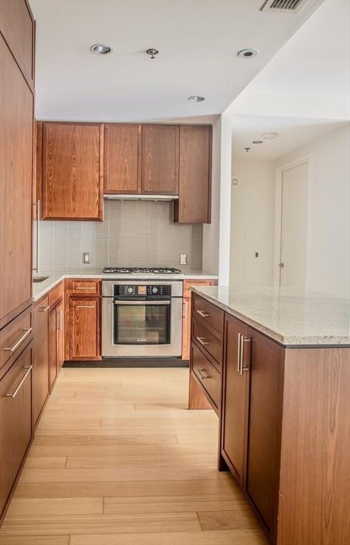 kitchen featuring stainless steel appliances, light hardwood / wood-style flooring, tasteful backsplash, and light stone counters