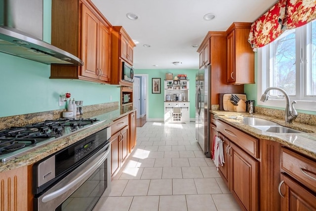 kitchen with light tile patterned floors, sink, stainless steel appliances, wall chimney exhaust hood, and light stone countertops