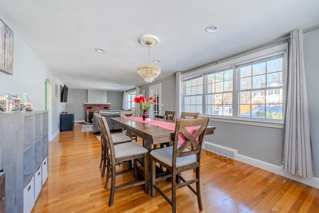 dining space featuring light hardwood / wood-style flooring, a chandelier, and a brick fireplace