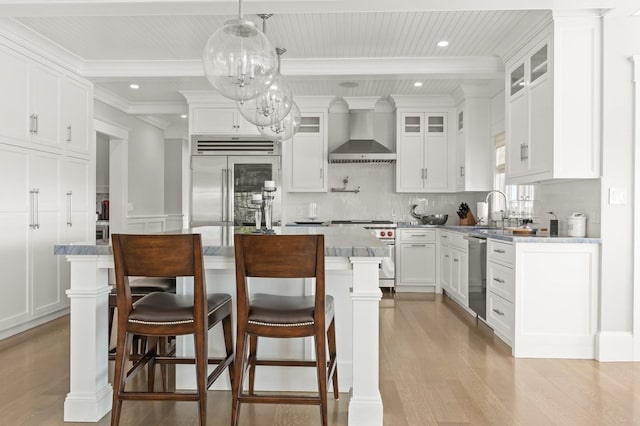 kitchen featuring a center island, wall chimney exhaust hood, decorative light fixtures, high quality appliances, and white cabinets