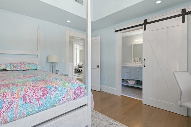 bedroom with a barn door, hardwood / wood-style flooring, and ensuite bath