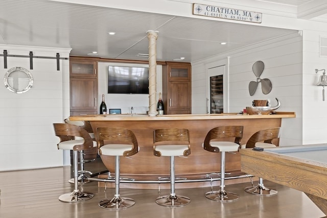 bar with a barn door, crown molding, and wooden walls