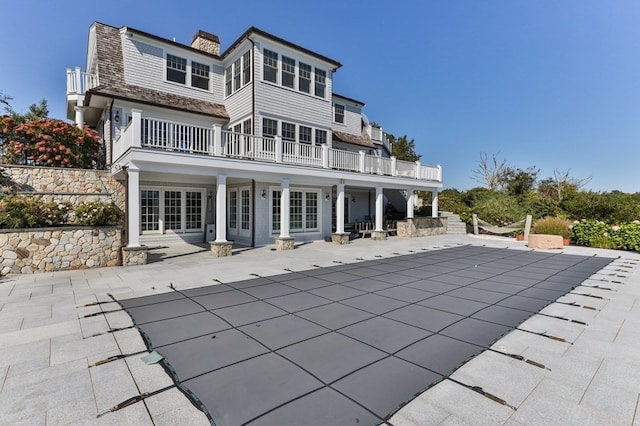 rear view of property with a covered pool, a balcony, a patio, and french doors