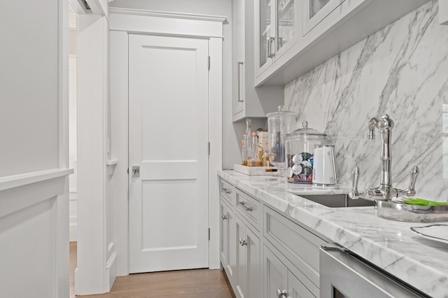 bar featuring light wood-type flooring, light stone counters, white cabinetry, and sink