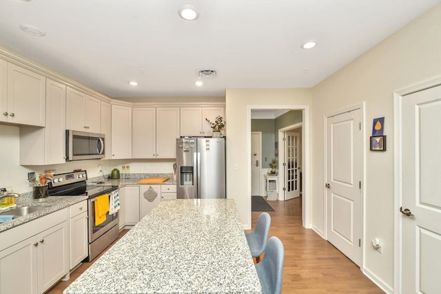 110 Trotter Rd Unit 104, Weymouth, MA 02190 - kitchen with stainless steel appliances, light stone counters, light wood-style floors, recessed lighting, and a breakfast bar