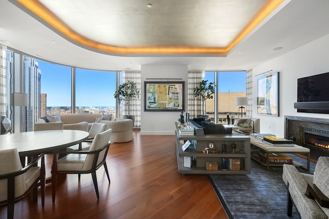 living room featuring a tray ceiling, a healthy amount of sunlight, dark hardwood / wood-style floors, and a high end fireplace