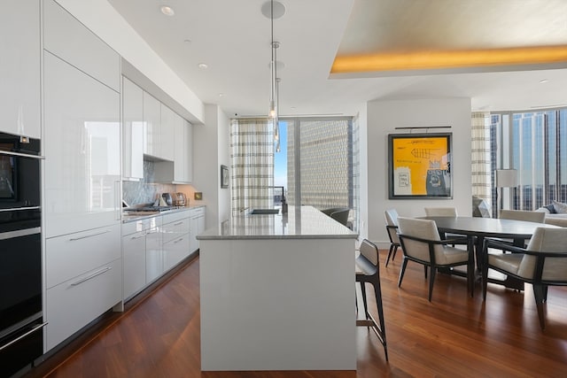 kitchen featuring decorative light fixtures, dark wood-type flooring, a kitchen island with sink, and white cabinetry