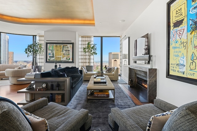 living room featuring a high end fireplace, a tray ceiling, dark hardwood / wood-style flooring, and a wall of windows