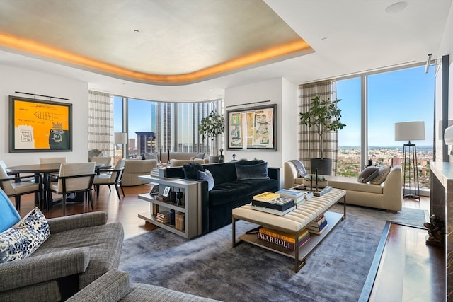 living room featuring dark wood-type flooring, a tray ceiling, and a wall of windows