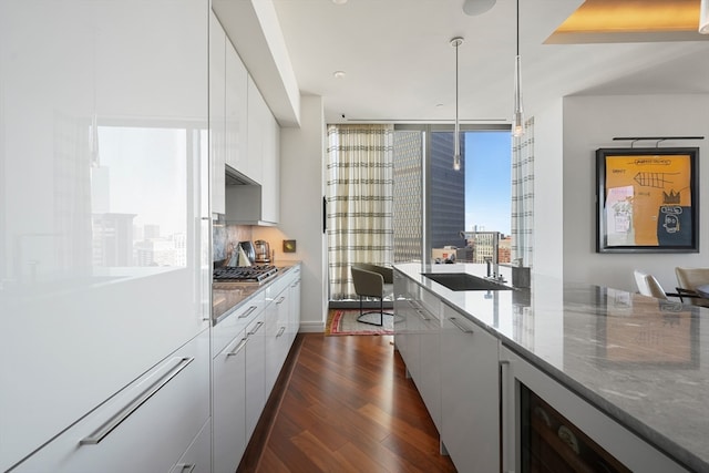 kitchen featuring stainless steel gas stovetop, dark hardwood / wood-style floors, light stone countertops, decorative light fixtures, and sink