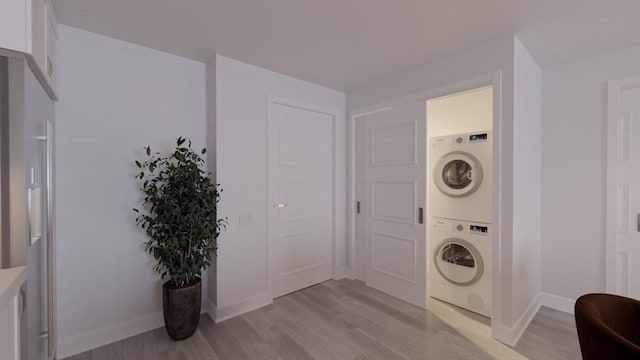 washroom featuring light wood finished floors, laundry area, stacked washer / drying machine, and baseboards