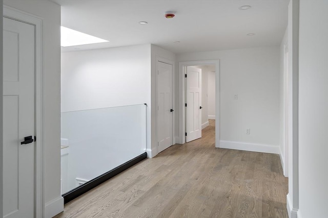 empty room with a skylight, light wood-style floors, and baseboards