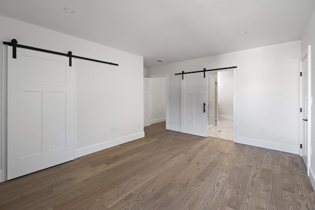unfurnished bedroom with a barn door, wood finished floors, and baseboards