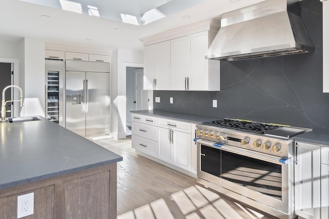 kitchen featuring high quality appliances, light wood-style floors, white cabinets, wall chimney exhaust hood, and a sink
