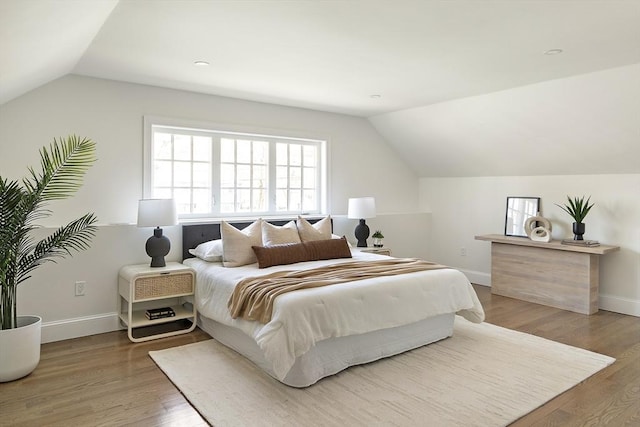 bedroom with baseboards, lofted ceiling, and wood finished floors