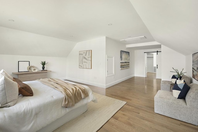 bedroom with a barn door, wood finished floors, baseboards, and lofted ceiling