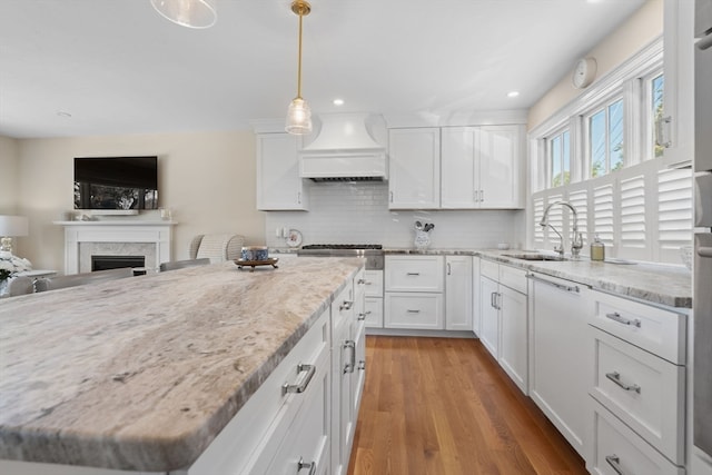 kitchen with dishwasher, hardwood / wood-style flooring, sink, white cabinetry, and premium range hood