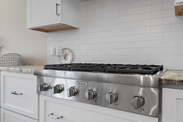 interior details featuring stainless steel gas cooktop, white cabinets, and backsplash