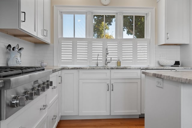 kitchen with sink, light stone countertops, stainless steel gas stovetop, white cabinets, and light hardwood / wood-style floors