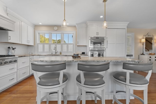 kitchen featuring white cabinetry, light hardwood / wood-style flooring, appliances with stainless steel finishes, and decorative light fixtures