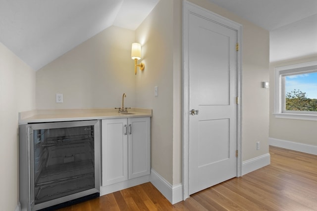 bar with lofted ceiling, white cabinets, beverage cooler, and light wood-type flooring