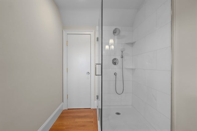 bathroom with a tile shower, hardwood / wood-style floors, and vaulted ceiling