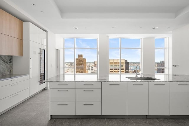 kitchen featuring white cabinetry, light stone countertops, sink, and light brown cabinetry