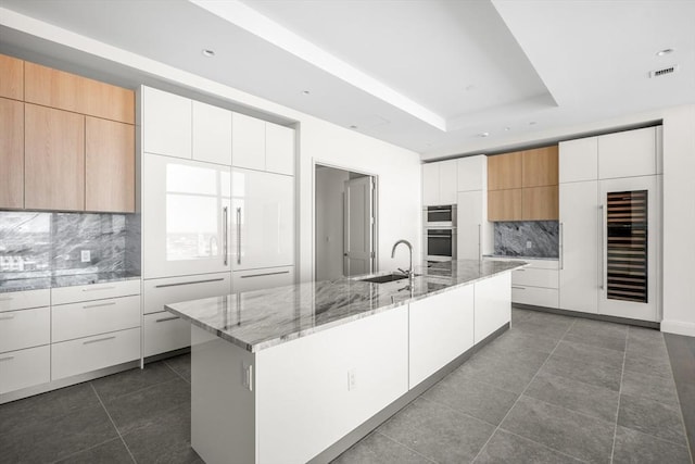 kitchen with a kitchen island with sink, sink, wine cooler, and white cabinets