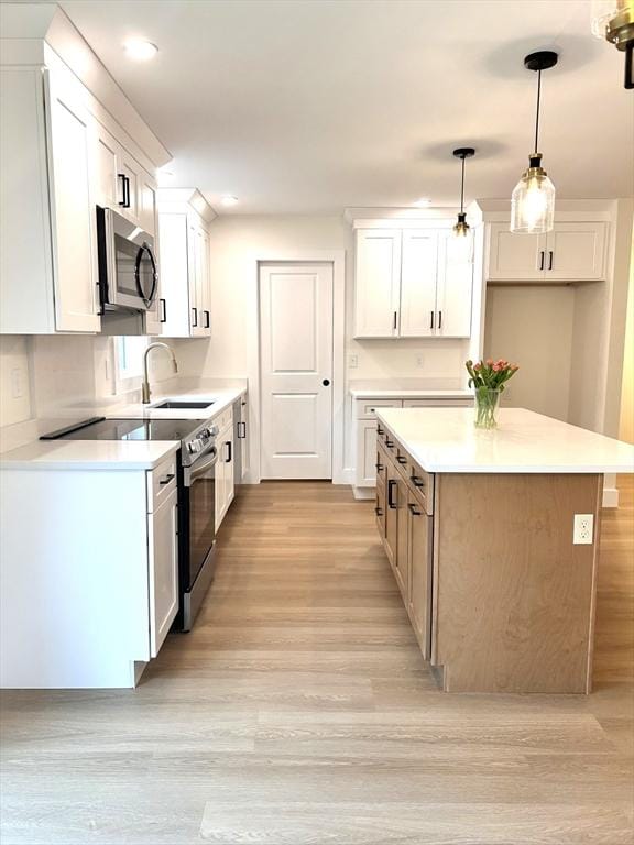 kitchen with light wood-style flooring, white cabinetry, a kitchen island, stainless steel microwave, and a sink