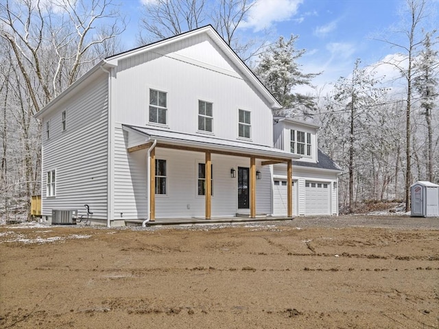 view of front of house featuring dirt driveway, cooling unit, covered porch, and a garage