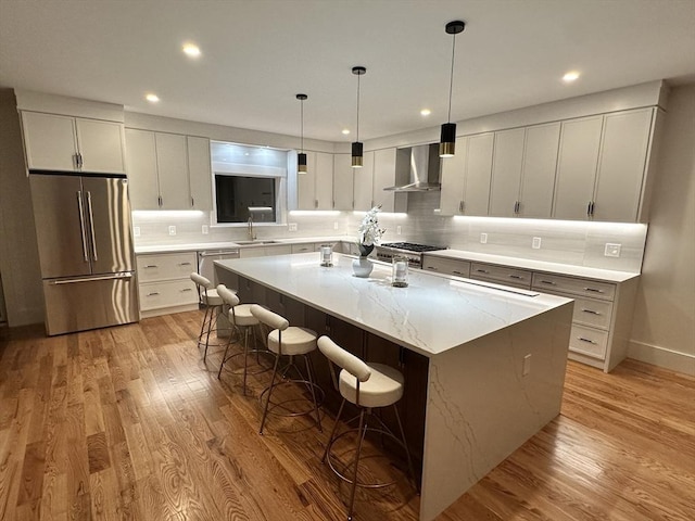 kitchen featuring a large island with sink, appliances with stainless steel finishes, wall chimney range hood, a breakfast bar area, and pendant lighting