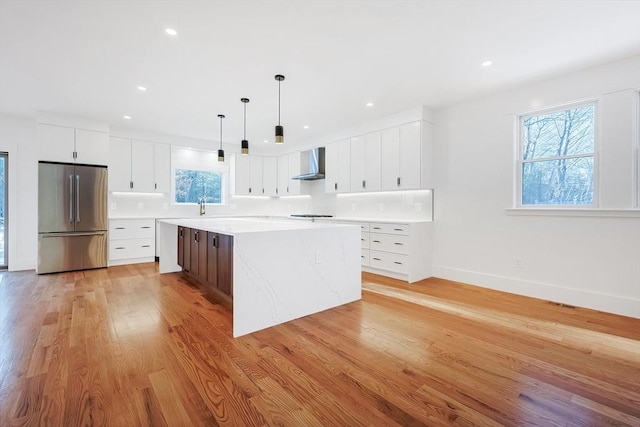 kitchen featuring a spacious island, white cabinets, stainless steel fridge, and wall chimney range hood